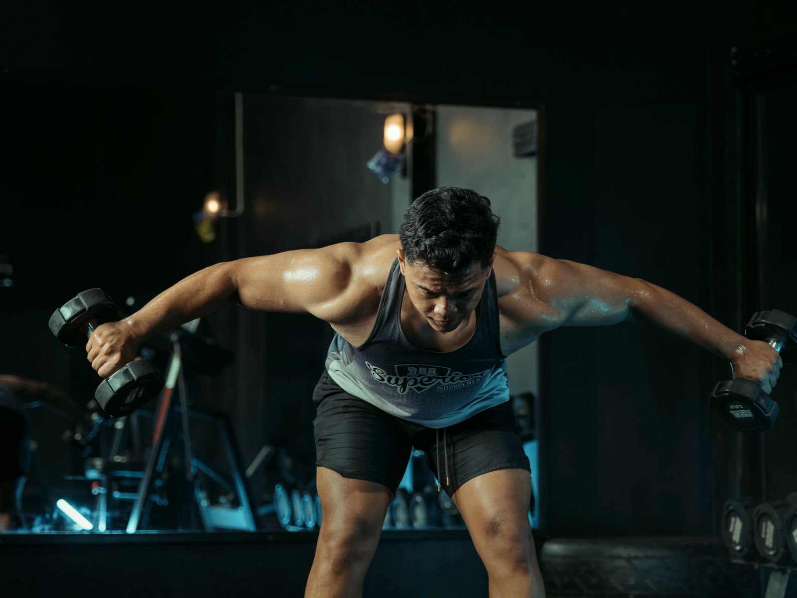 Homem realizando levantamento de halteres em academia dark.
